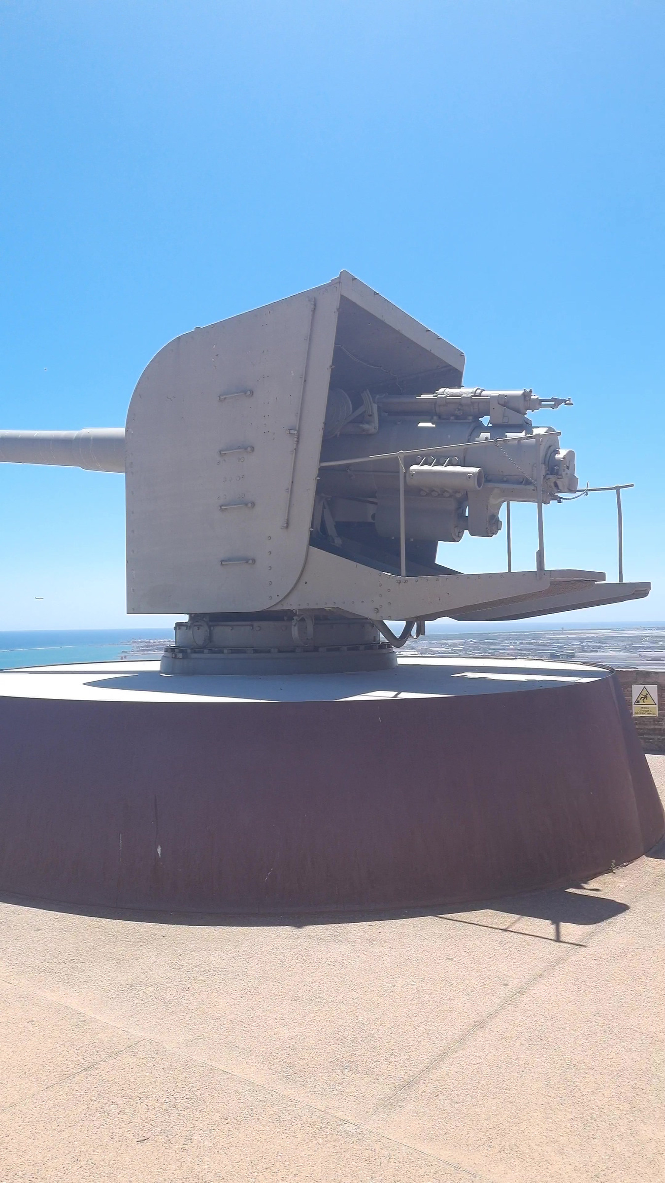 A grey gun turret on a round rust-coloured base under a blue sky.